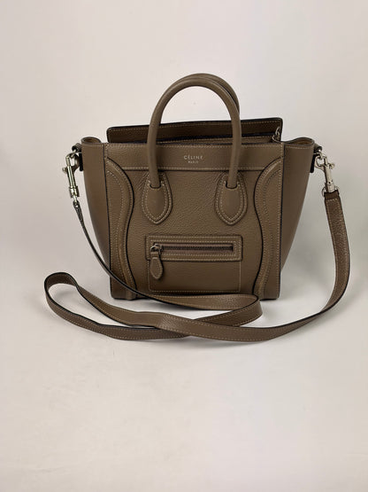 A taupe brown pebbled leather handbag with dual top handles, a front zip pocket, and a matching shoulder strap, photographed against a neutral off-white background.