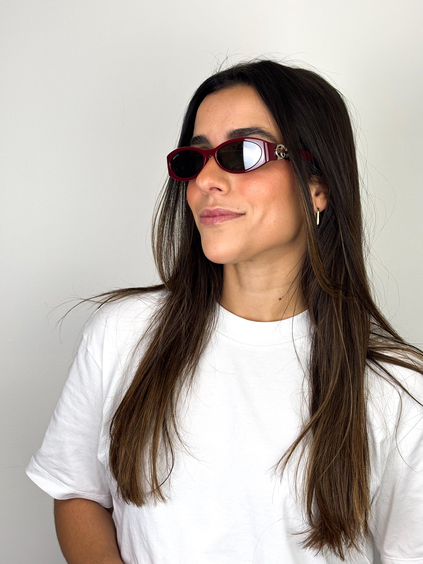 Woman wearing red sunglasses and a white t-shirt against a plain background